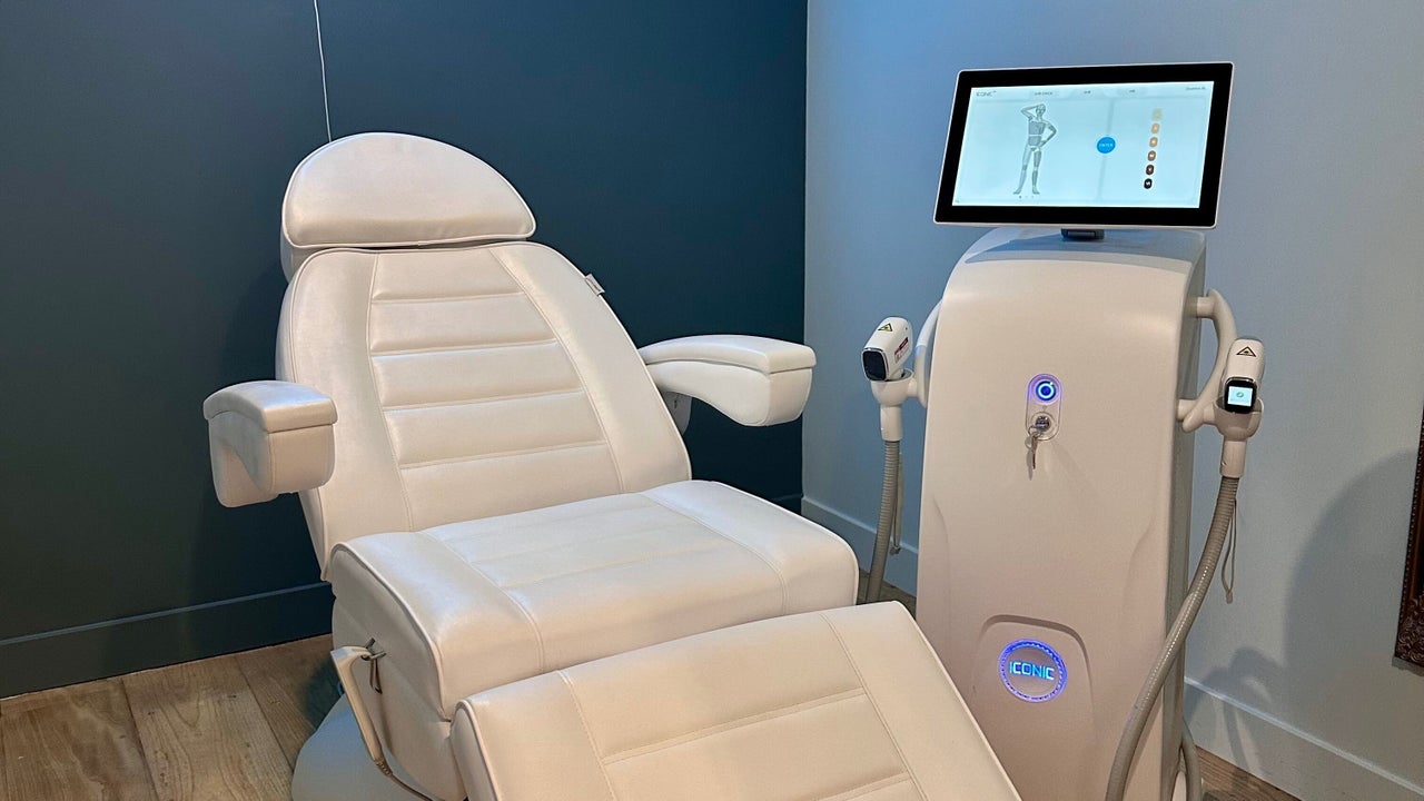 De witte behandelstoel naast het laserapparaat met touchscreen, tegen de donkere muur